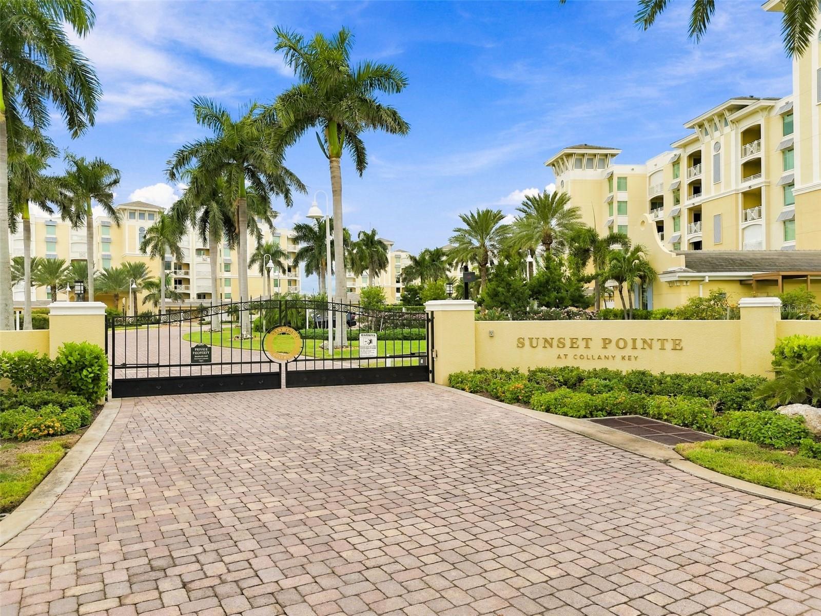 Gated Sunset Pointe at Collany Key entrance framed by palm trees and yellow condominium buildings.
