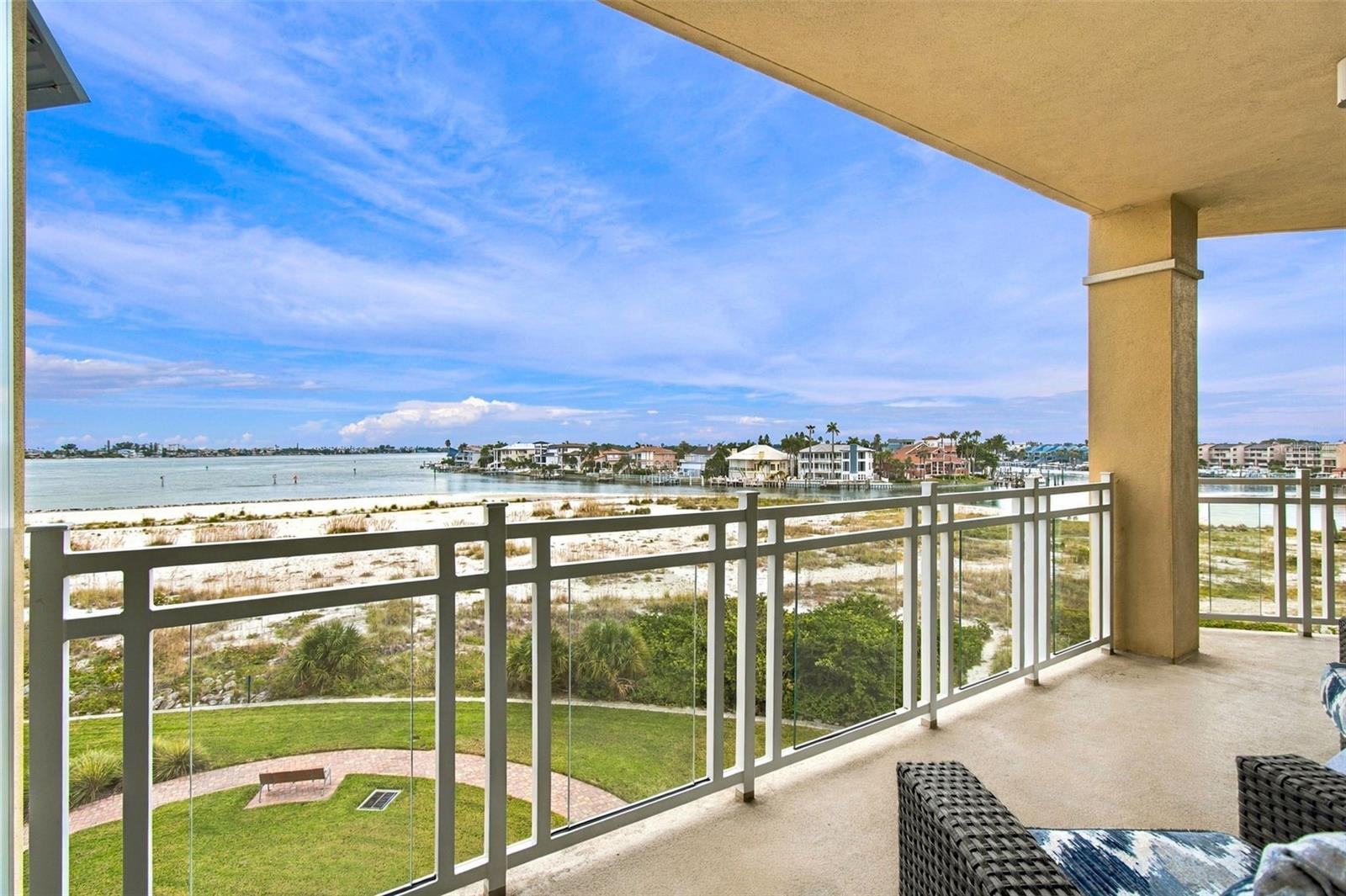 Covered balcony overlooking a sandy shoreline, calm bay, and waterfront homes.