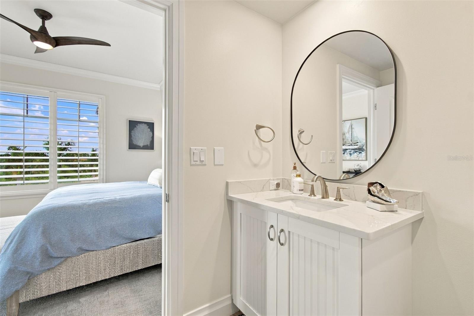 Bathroom vanity with an oval mirror beside a bedroom with a blue-covered bed.