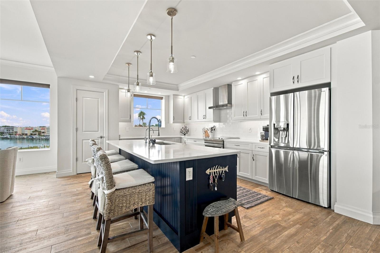 Bright condo kitchen with white cabinets, stainless appliances, navy island, and water views.