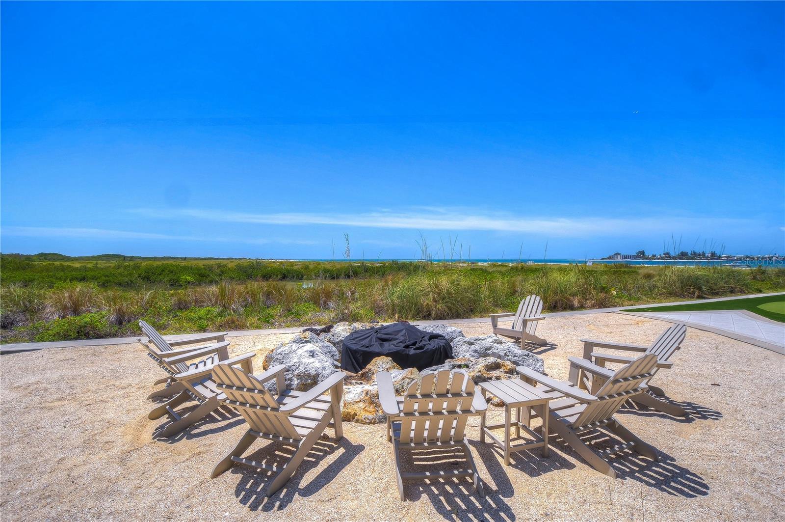 Outdoor patio with Adirondack chairs facing coastal dunes and water.