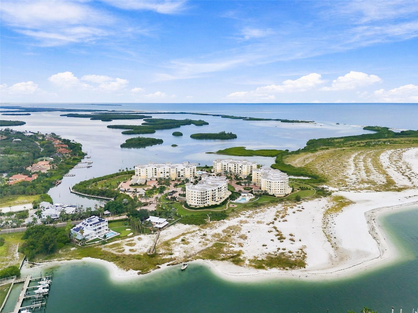 Waterfront condominium complex on a sandy peninsula, with mangrove islands, beaches, and boat docks.