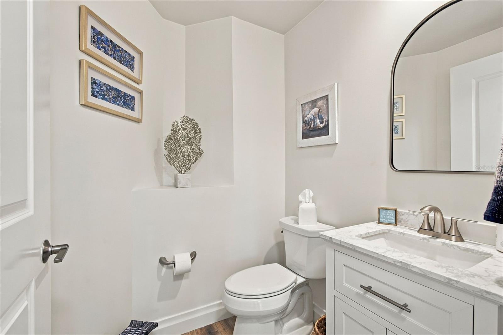 Bathroom with white vanity, marble-look countertop, large mirror, and framed wall art.