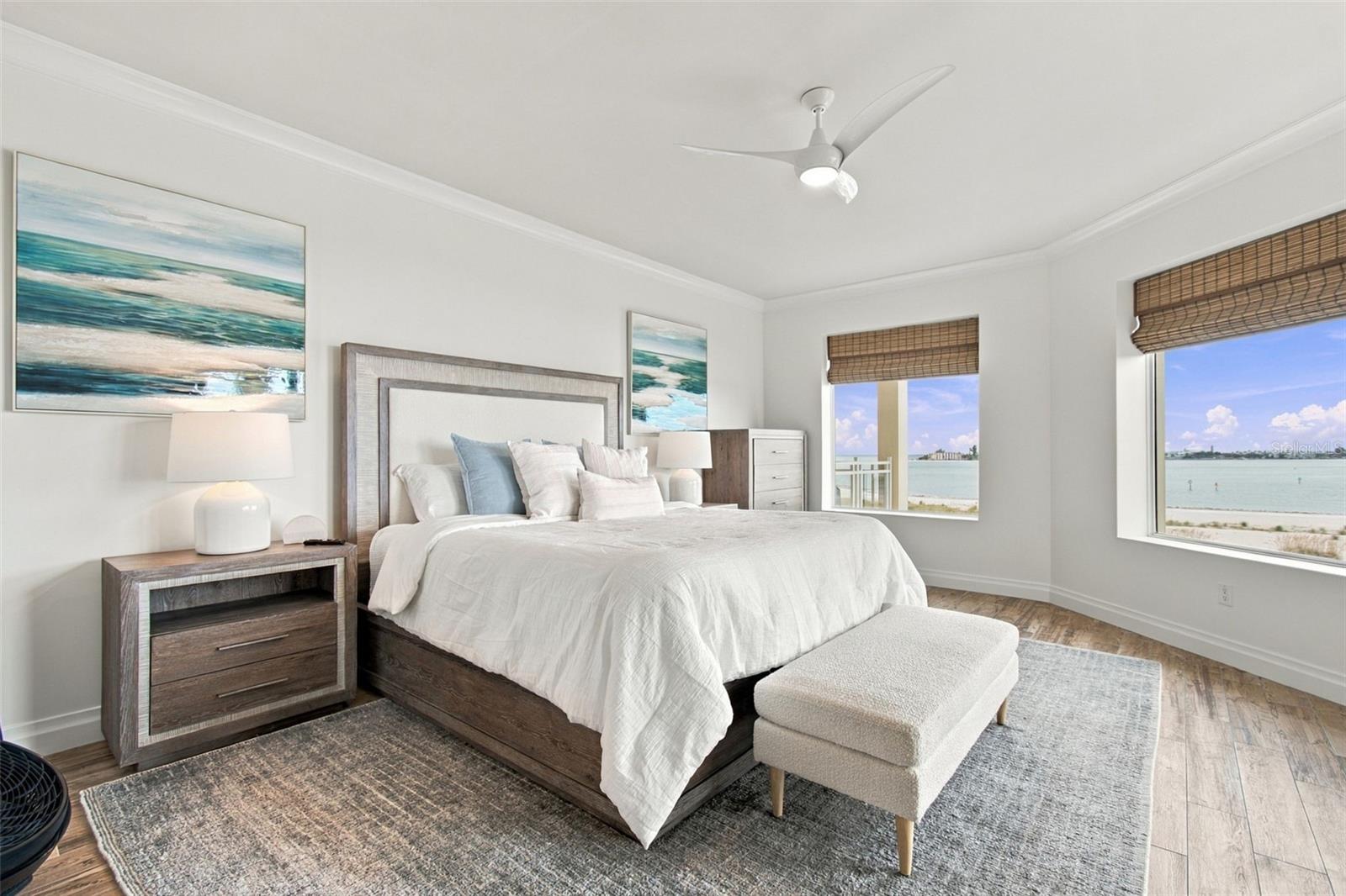Bedroom with a white bed and two windows overlooking the water.