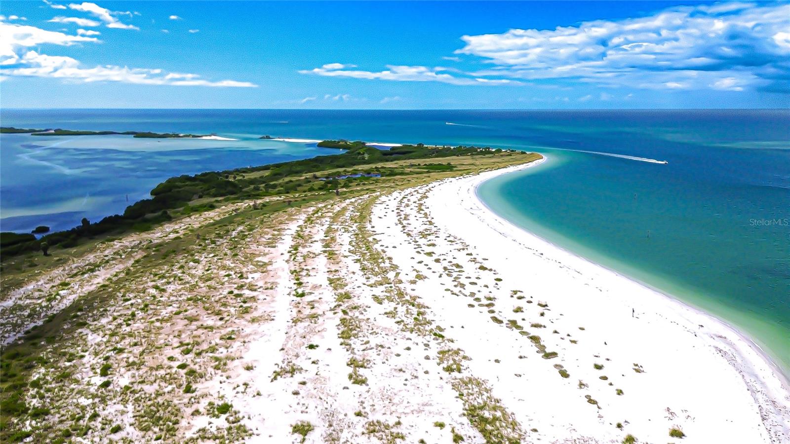 Aerial view of a curved white-sand beach between turquoise Gulf waters and a calm lagoon.