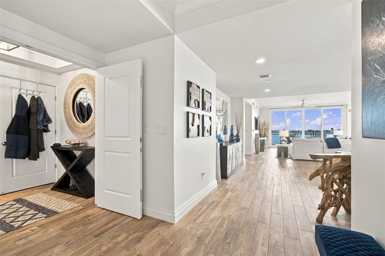 Condo entry hall opening to a furnished living room with water views through large windows.