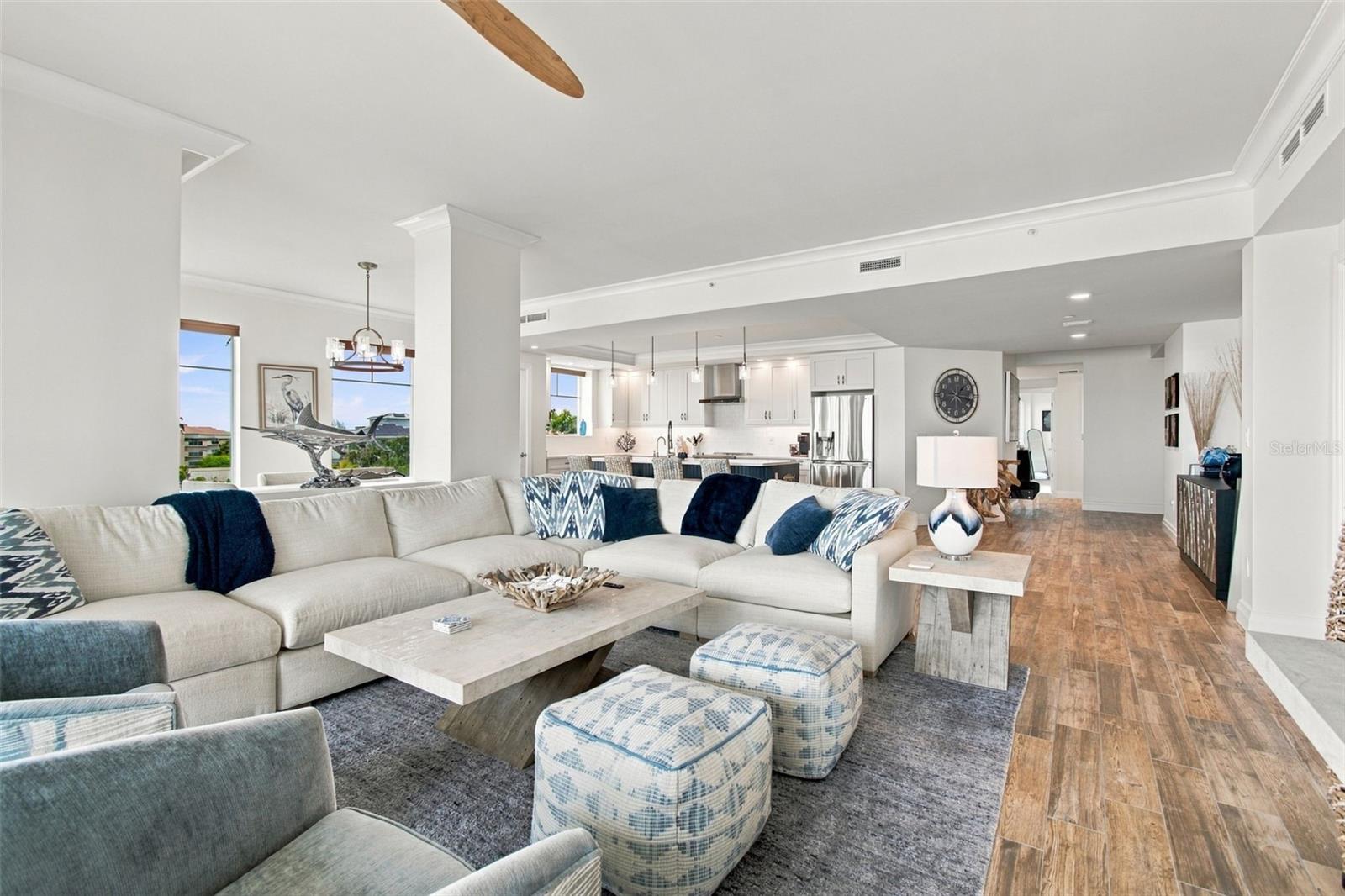 Open-plan living room with a large white sectional, patterned ottomans, and kitchen beyond.