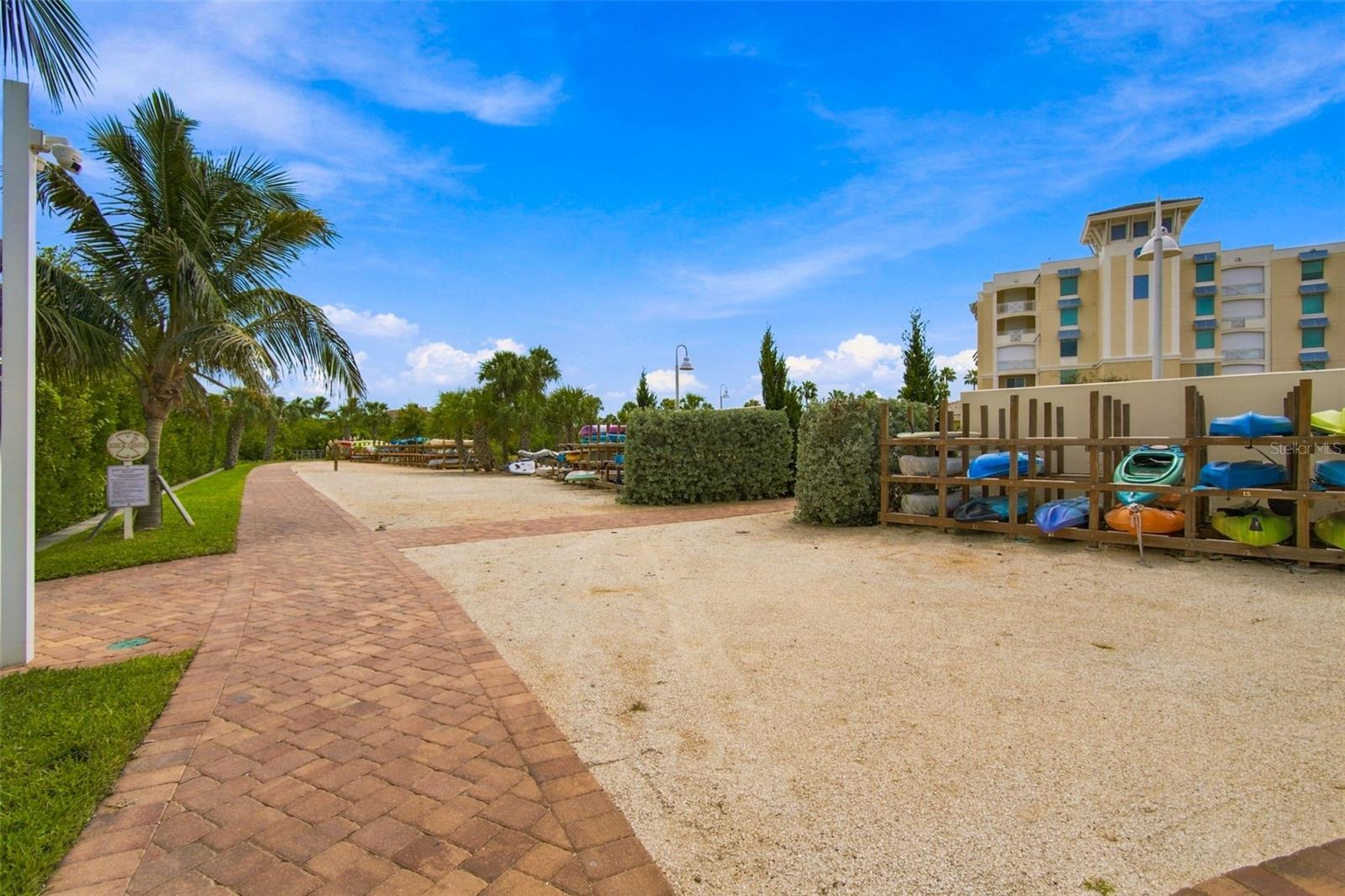 Condominium kayak storage area beside a brick walkway and palm trees.