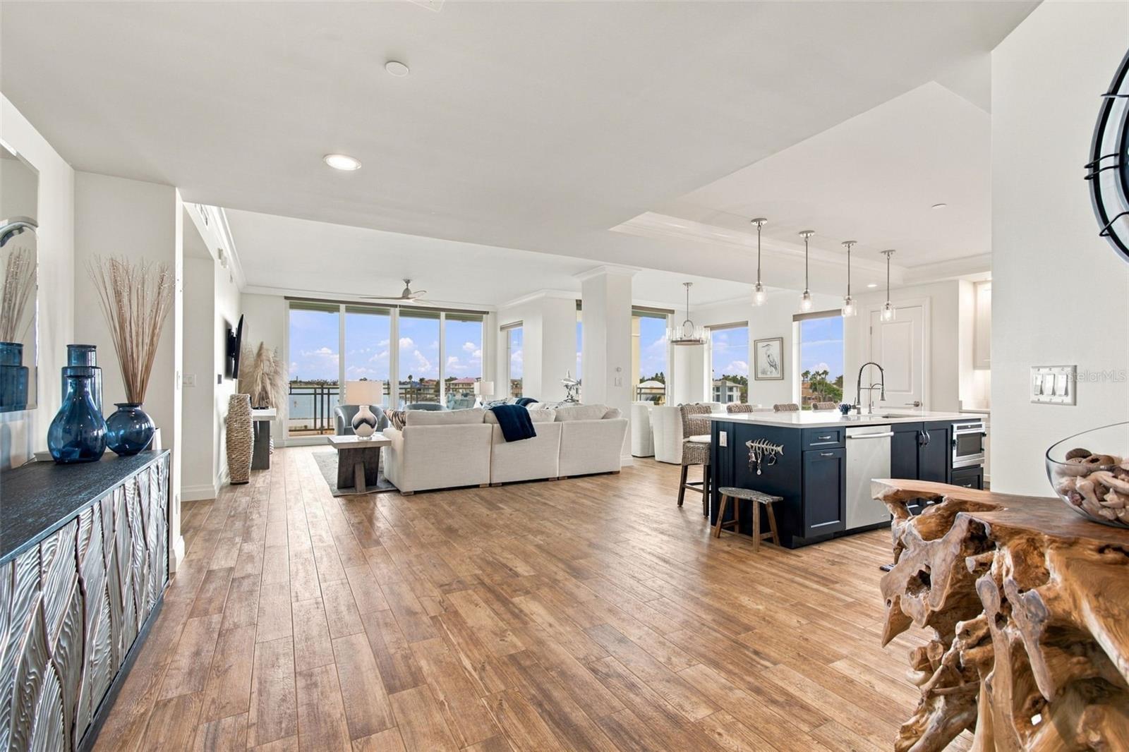 Open-plan living room and kitchen with a dark island, wood floors, and water views through large windows.