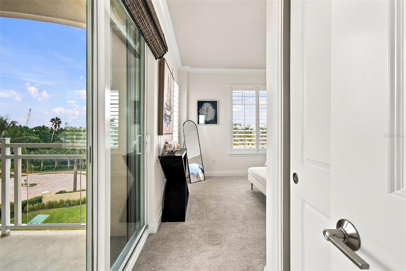 Bright carpeted bedroom with a sliding glass door to a balcony overlooking greenery.