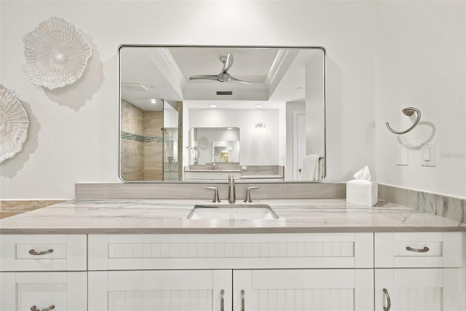 Bathroom vanity with a marble-pattern counter and large mirror reflecting a tiled shower.