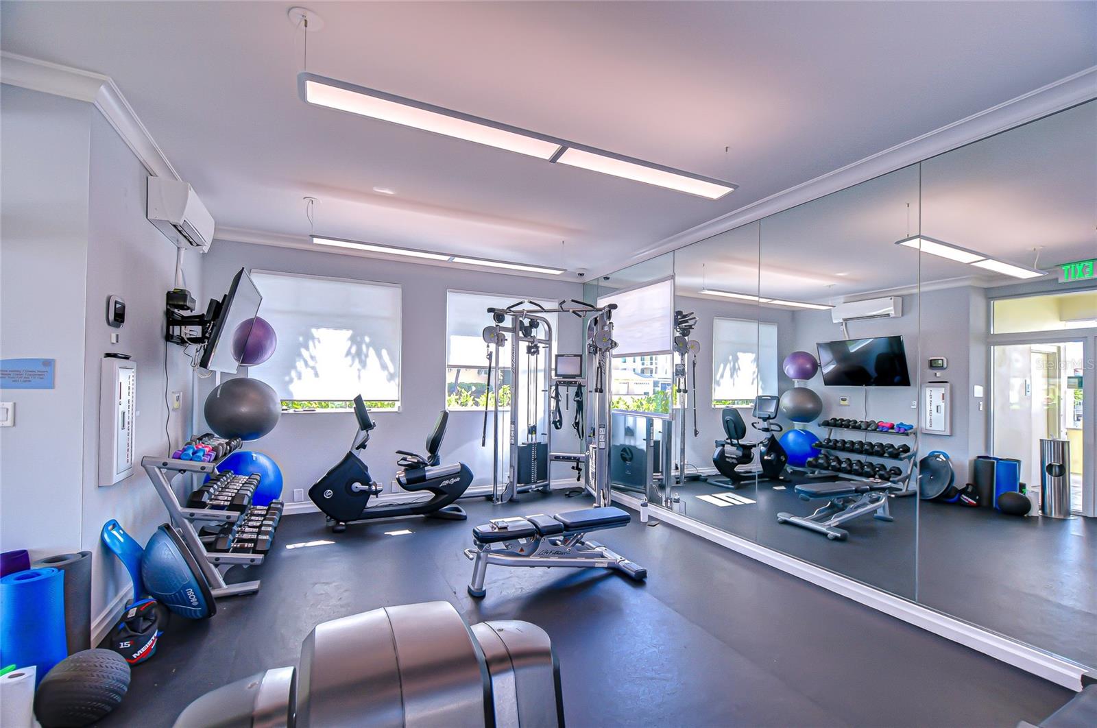 Fitness room with mirrored walls, weight machines, dumbbells, and exercise bikes.