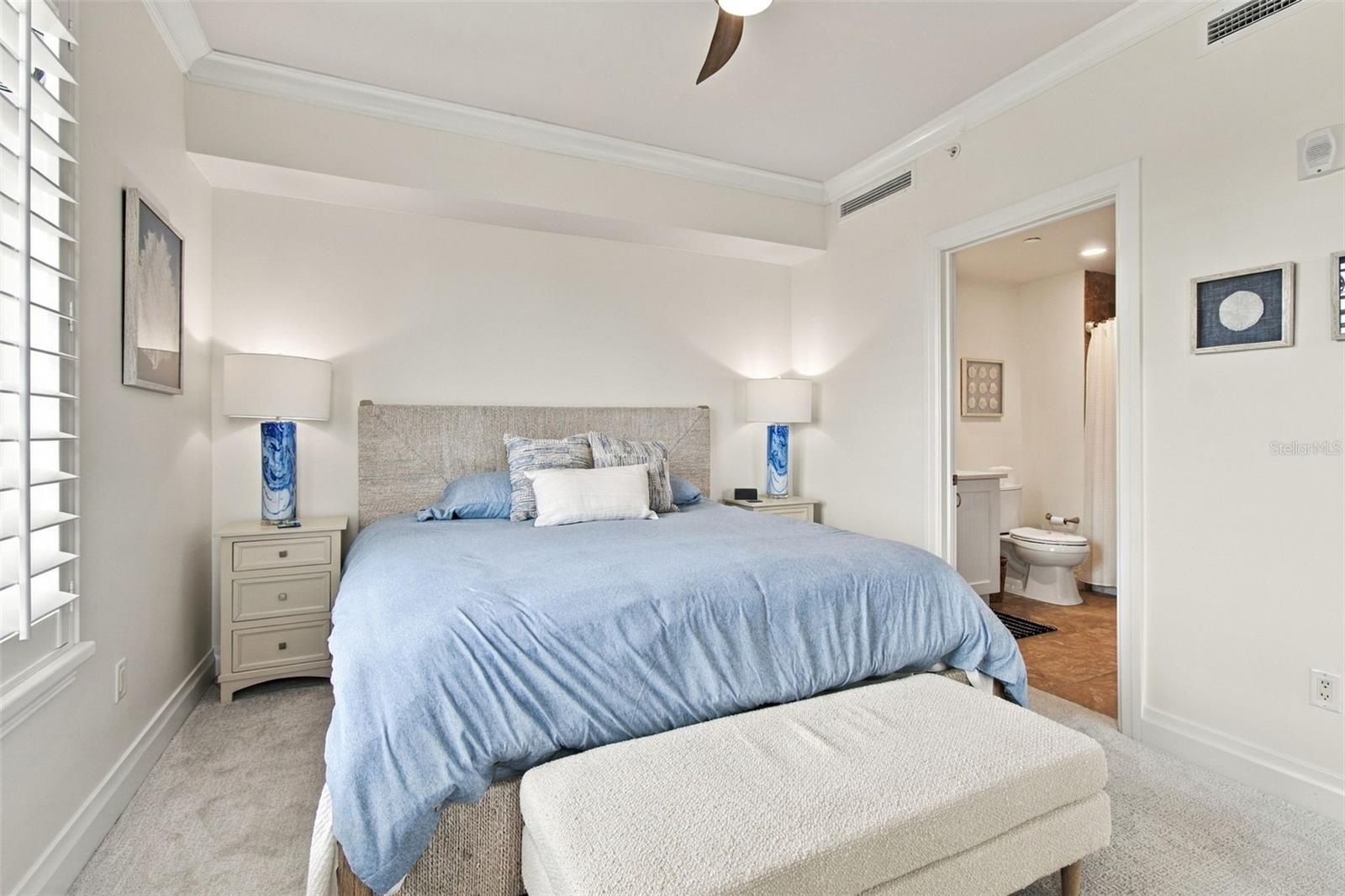 Bedroom with a blue-bedded king-size bed, upholstered bench, and adjoining bathroom.