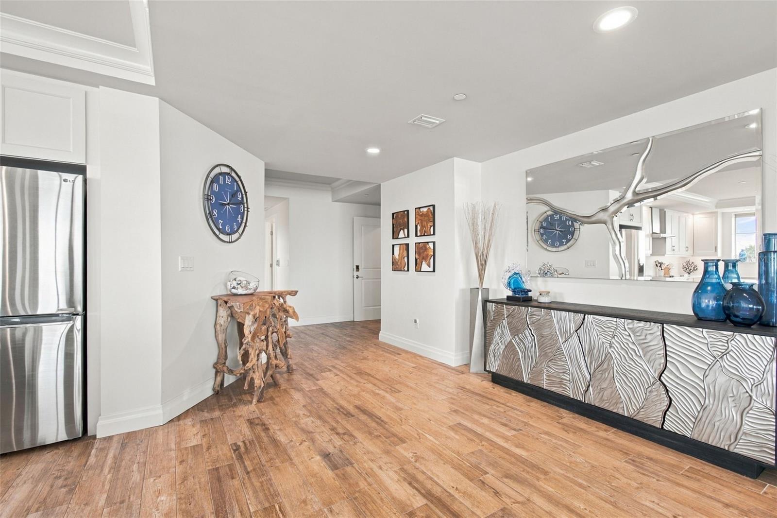 Condo entry with wood-look tile floors, sculptural console table, and large wavy-edged mirror.