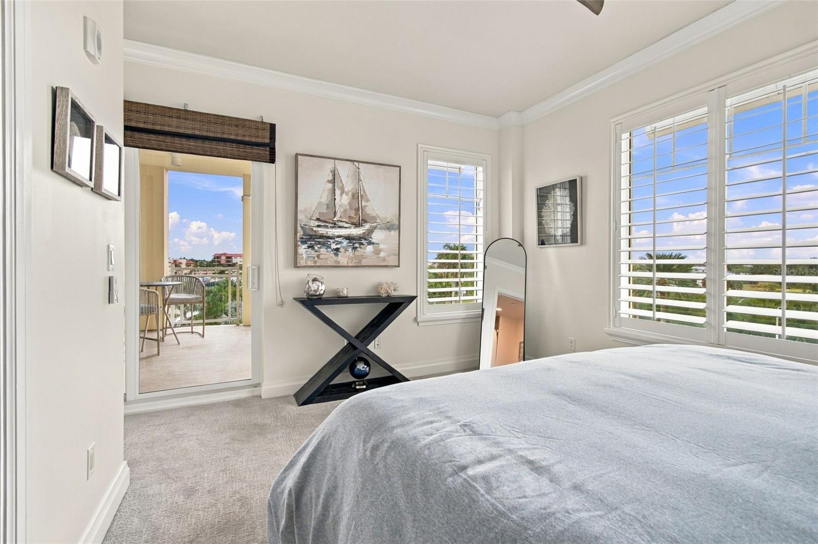 Bright bedroom with a gray bed, plantation shutters, and a balcony doorway.