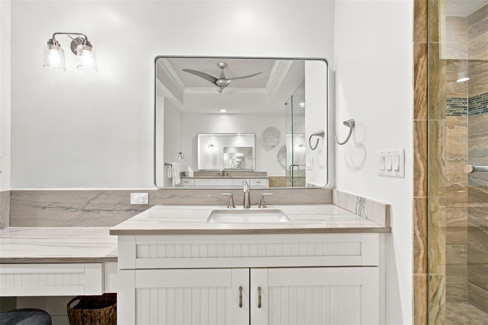 Bathroom vanity with veined stone counters, a large mirror, and a glass-enclosed tiled shower.