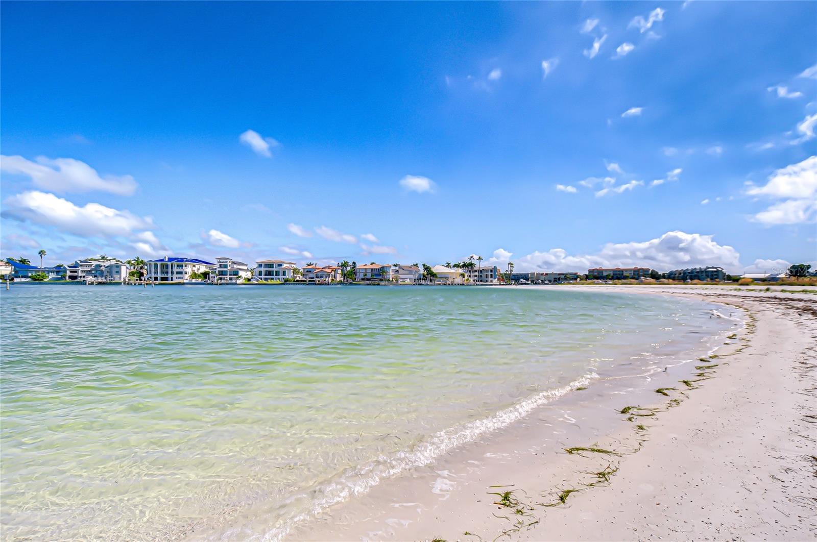 Sandy beach and shallow waterfront, with palm-lined homes across the bay.