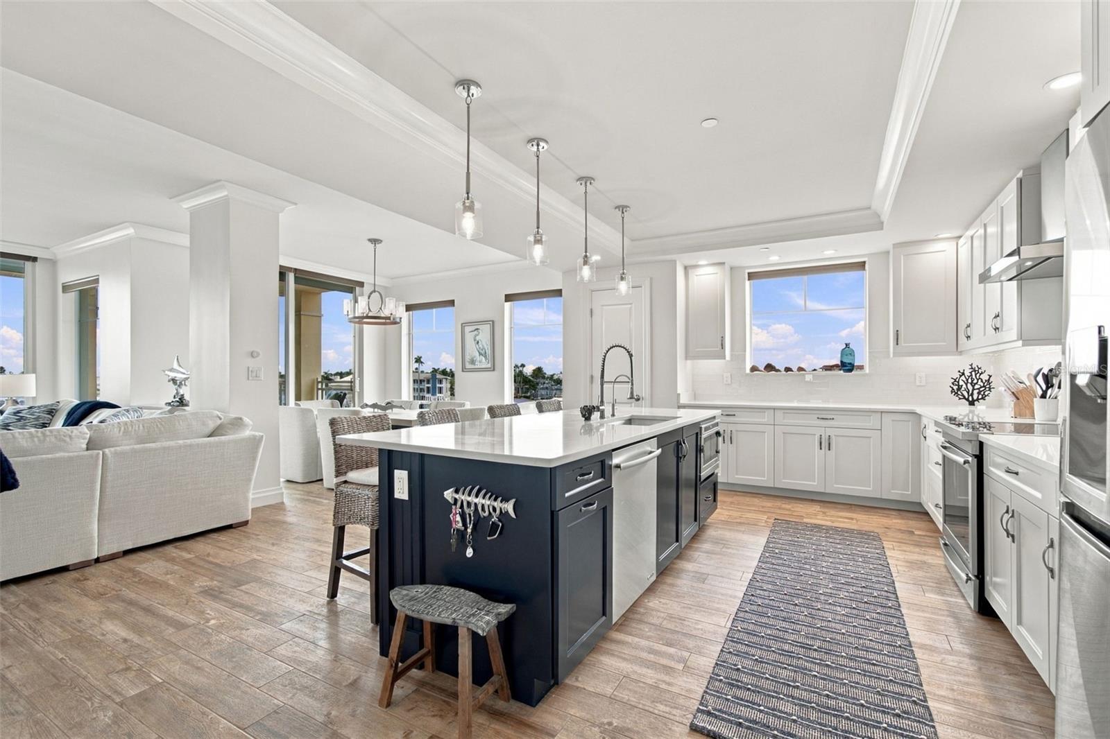Open-plan kitchen with a navy island, white cabinets, and water views through the windows.