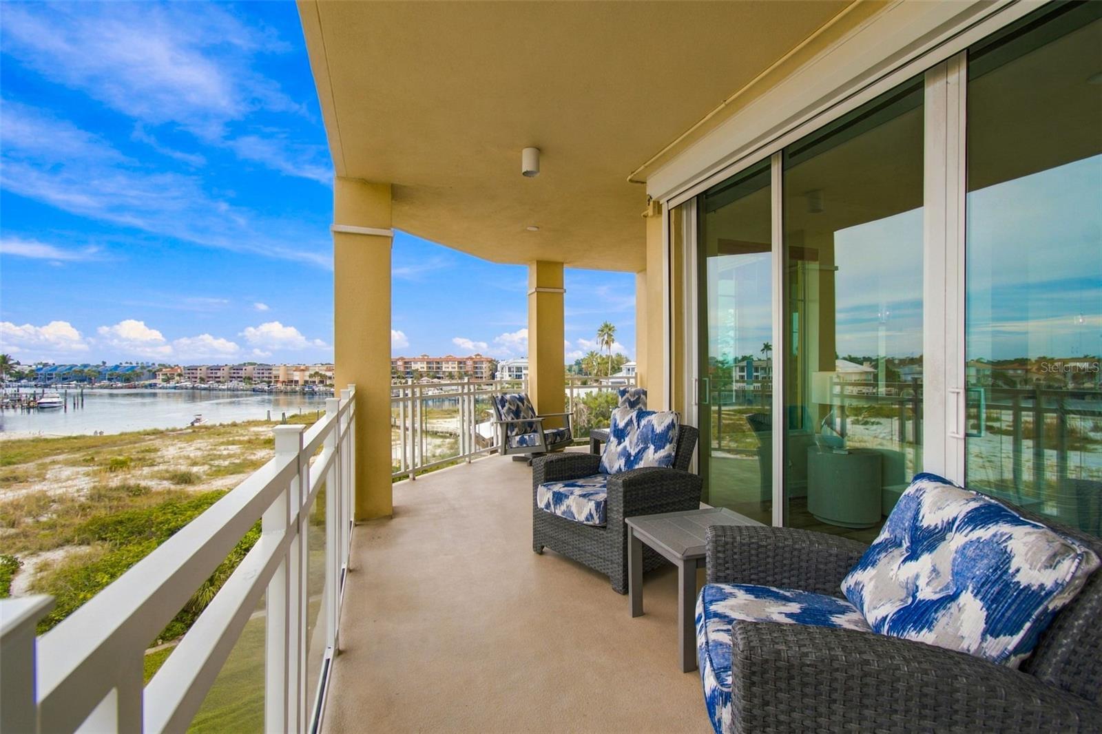 Condominium balcony with wicker seating overlooking a waterfront inlet and shoreline buildings.