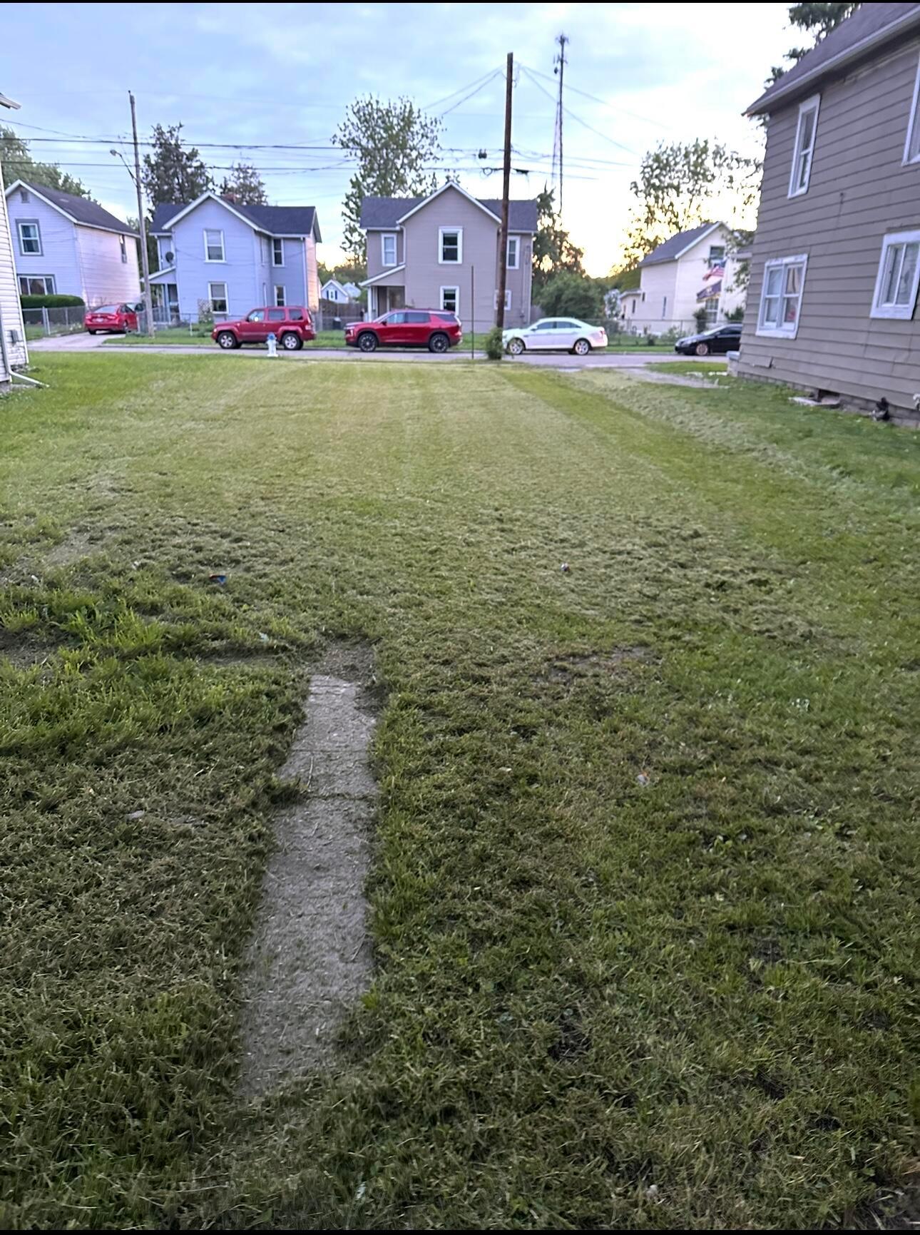Grassy front yard and concrete walkway facing two-story homes across a residential street.