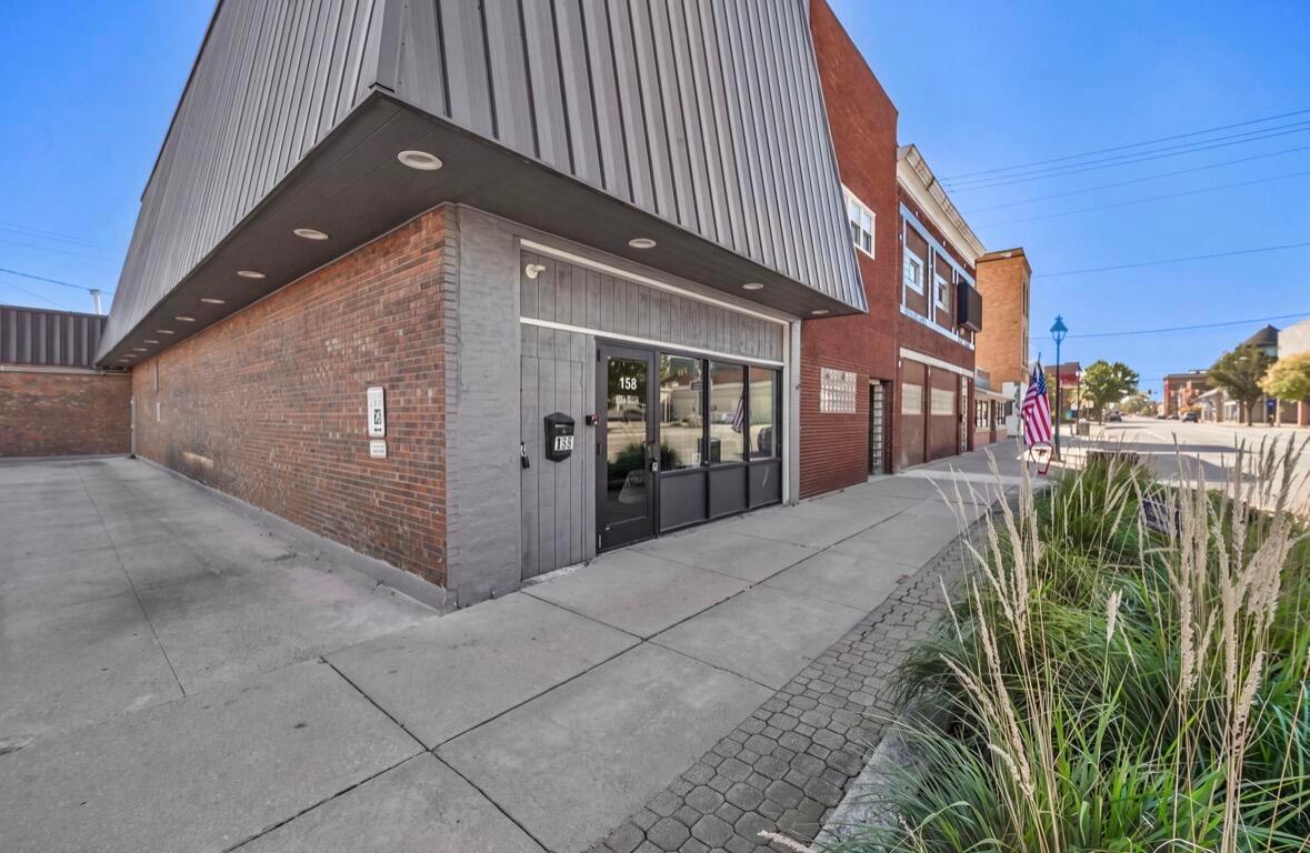 Brick downtown storefront at 158 with gray metal cladding, glass entry, and sidewalk grasses.