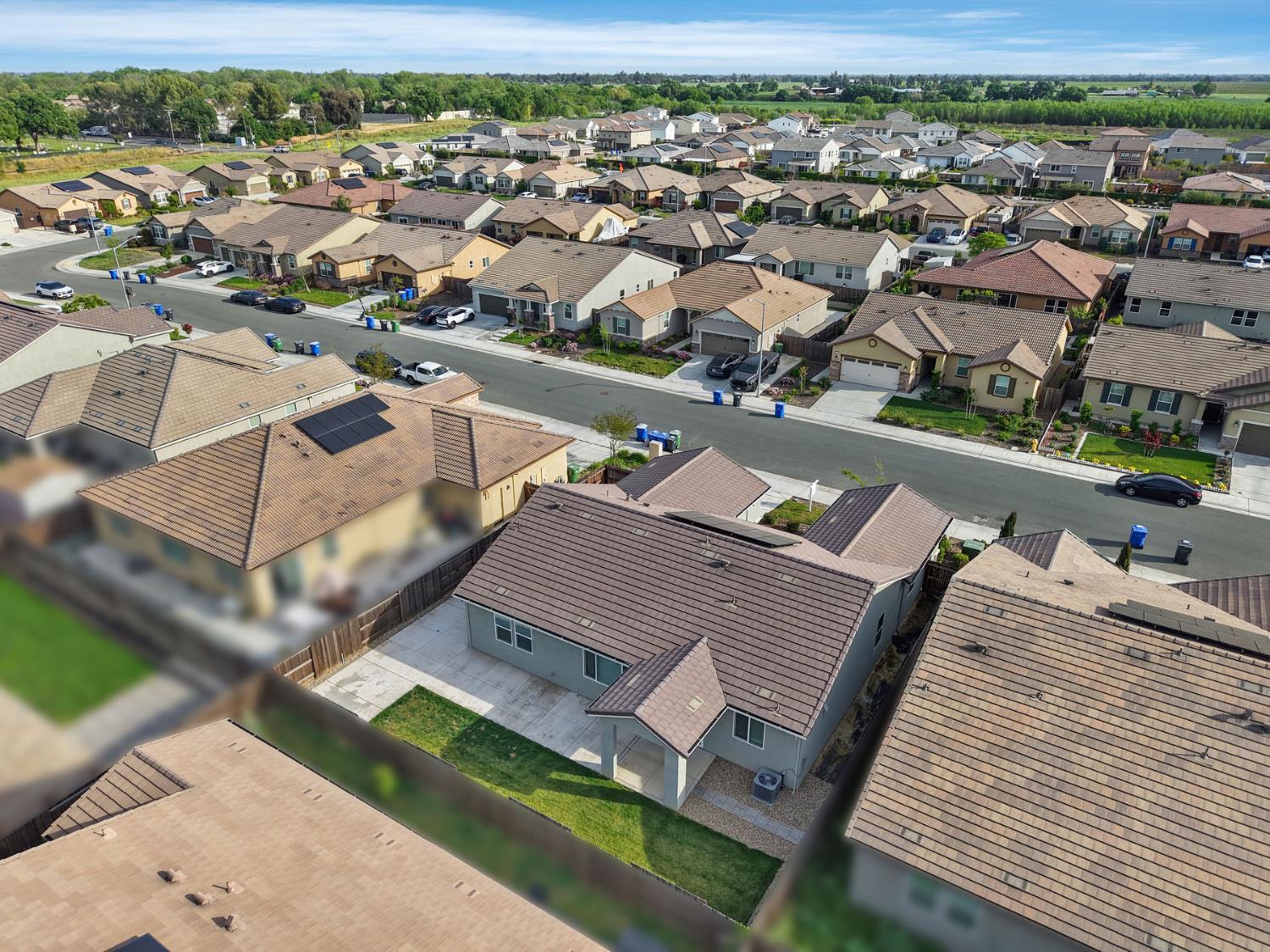 Aerial view of a residential neighborhood with single-story homes, a street, and fields on the horizon.