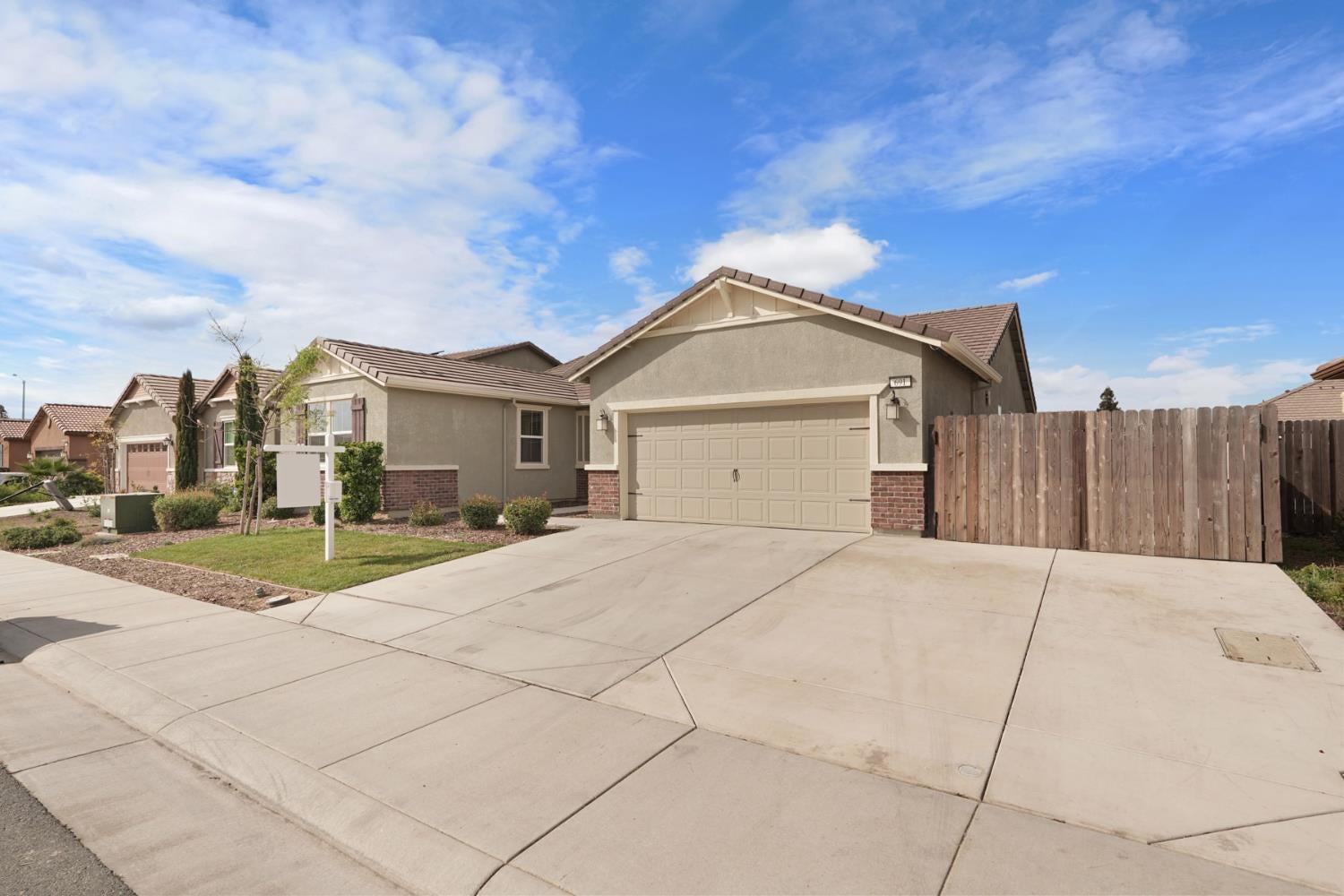 Single-story stucco home with a two-car garage, wide driveway, small front lawn, and wooden side fence.