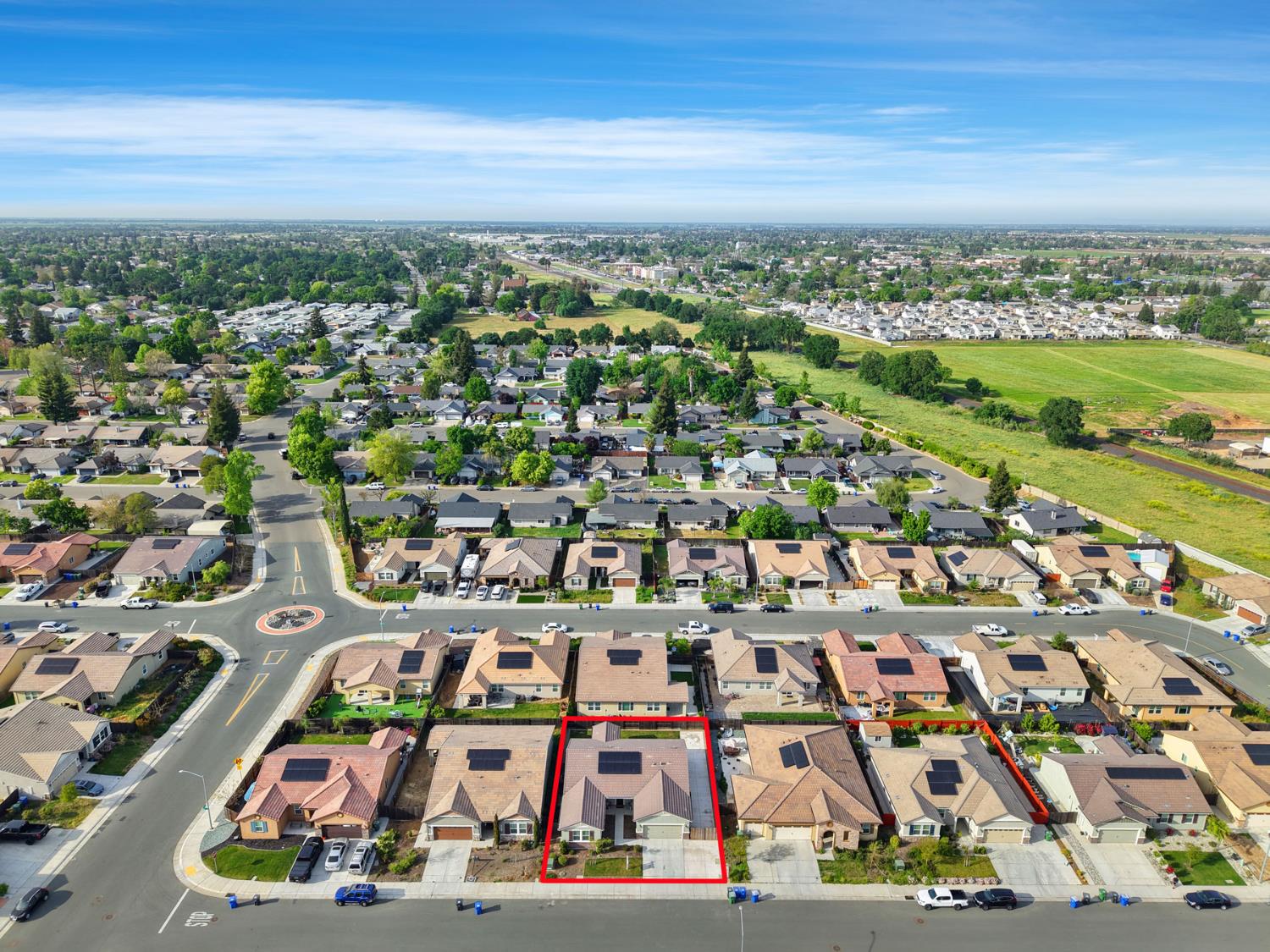 Aerial view of a single-story home outlined in red, with rooftop solar panels and neighboring houses.