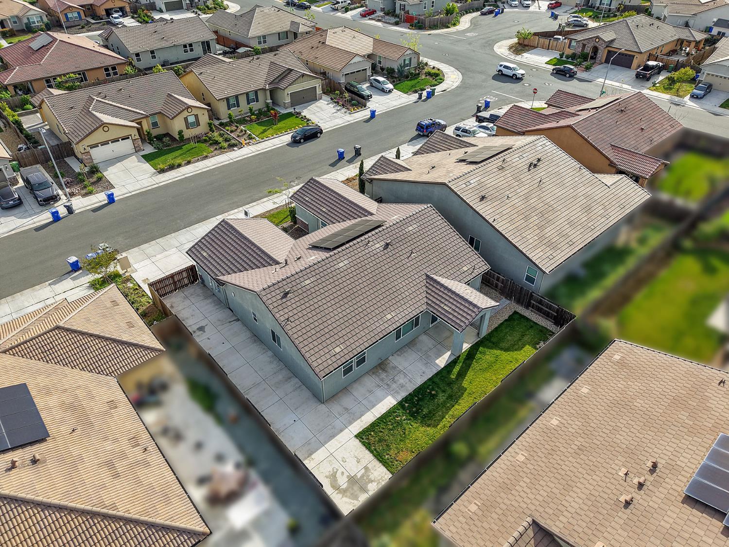Aerial view of a single-story home with a broad driveway, fenced yard, and surrounding homes.