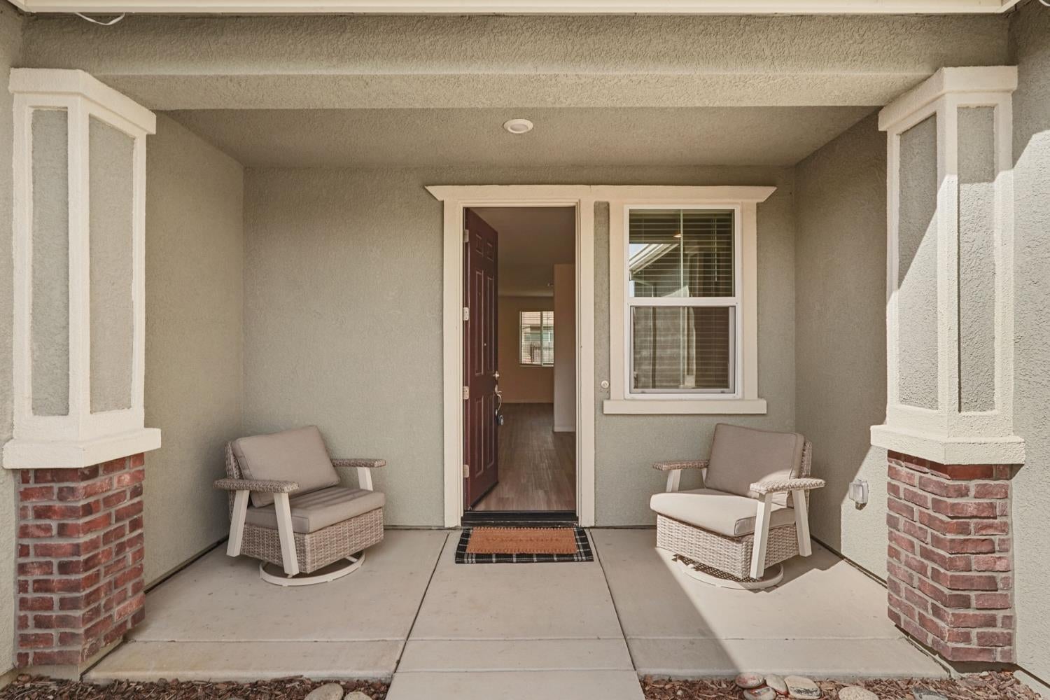 Covered front porch with two wicker chairs beside an open front door.