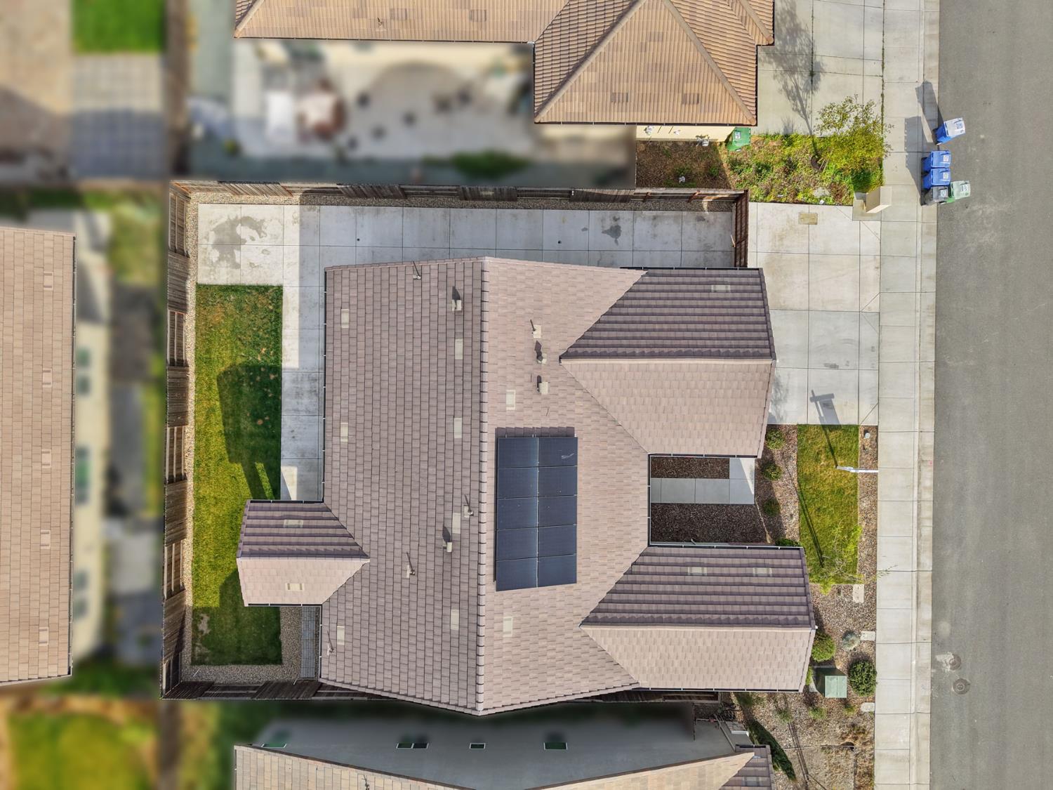 Aerial view of a home with rooftop solar panels, a fenced lawn, and paved side yard.