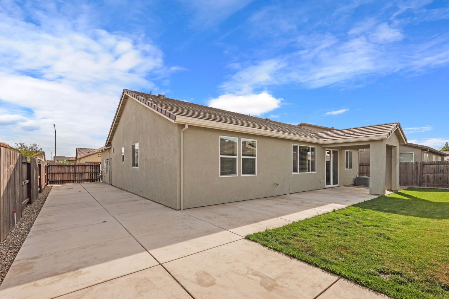 Rear of a stucco home with a covered patio, wide concrete terrace, fenced yard, and lawn.