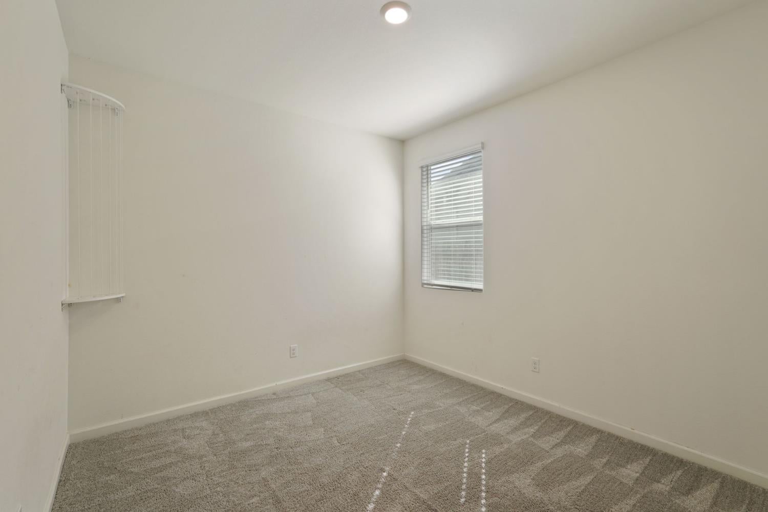 Empty bedroom with gray carpet, a window with blinds, and a short white railing.