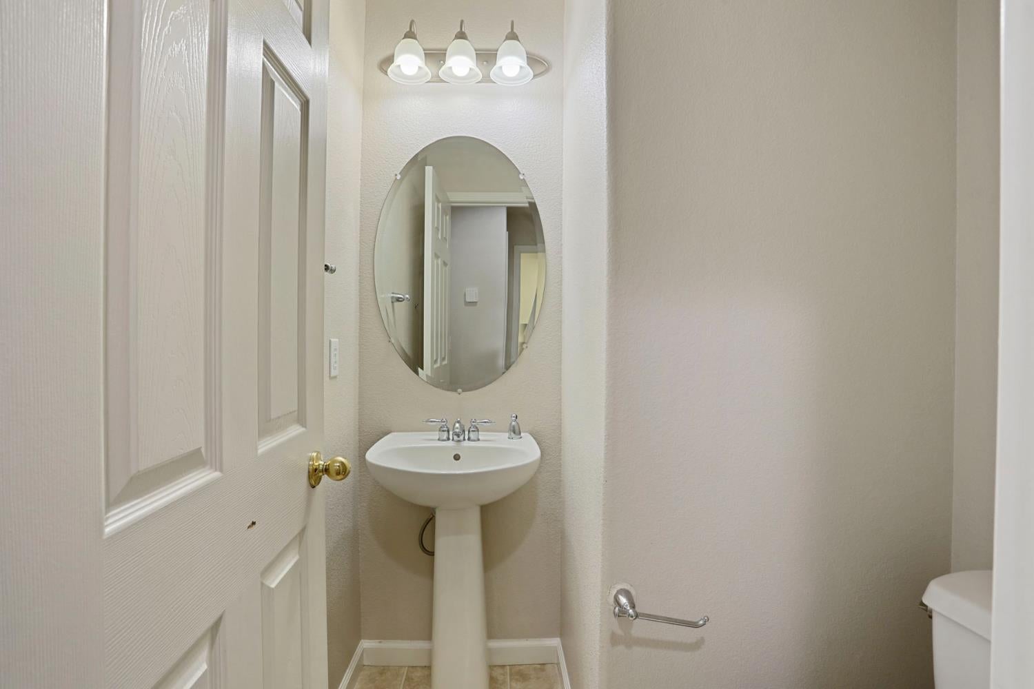 Bathroom with a pedestal sink, oval mirror, and three-light fixture.