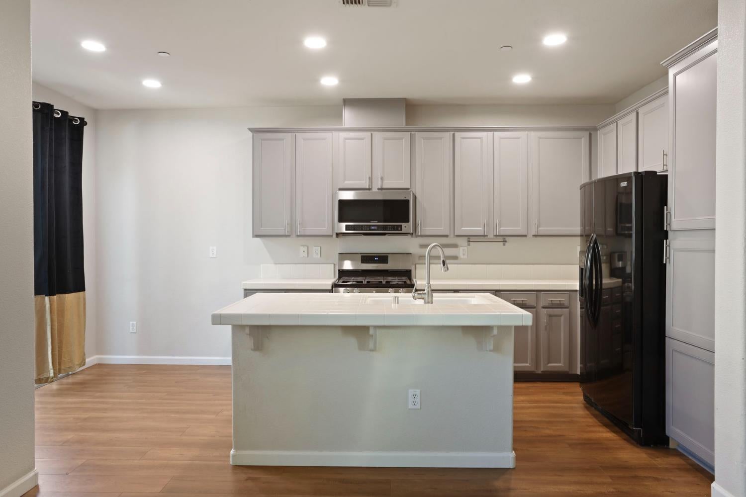 Kitchen with a large tiled island, white cabinets, and stainless steel appliances.