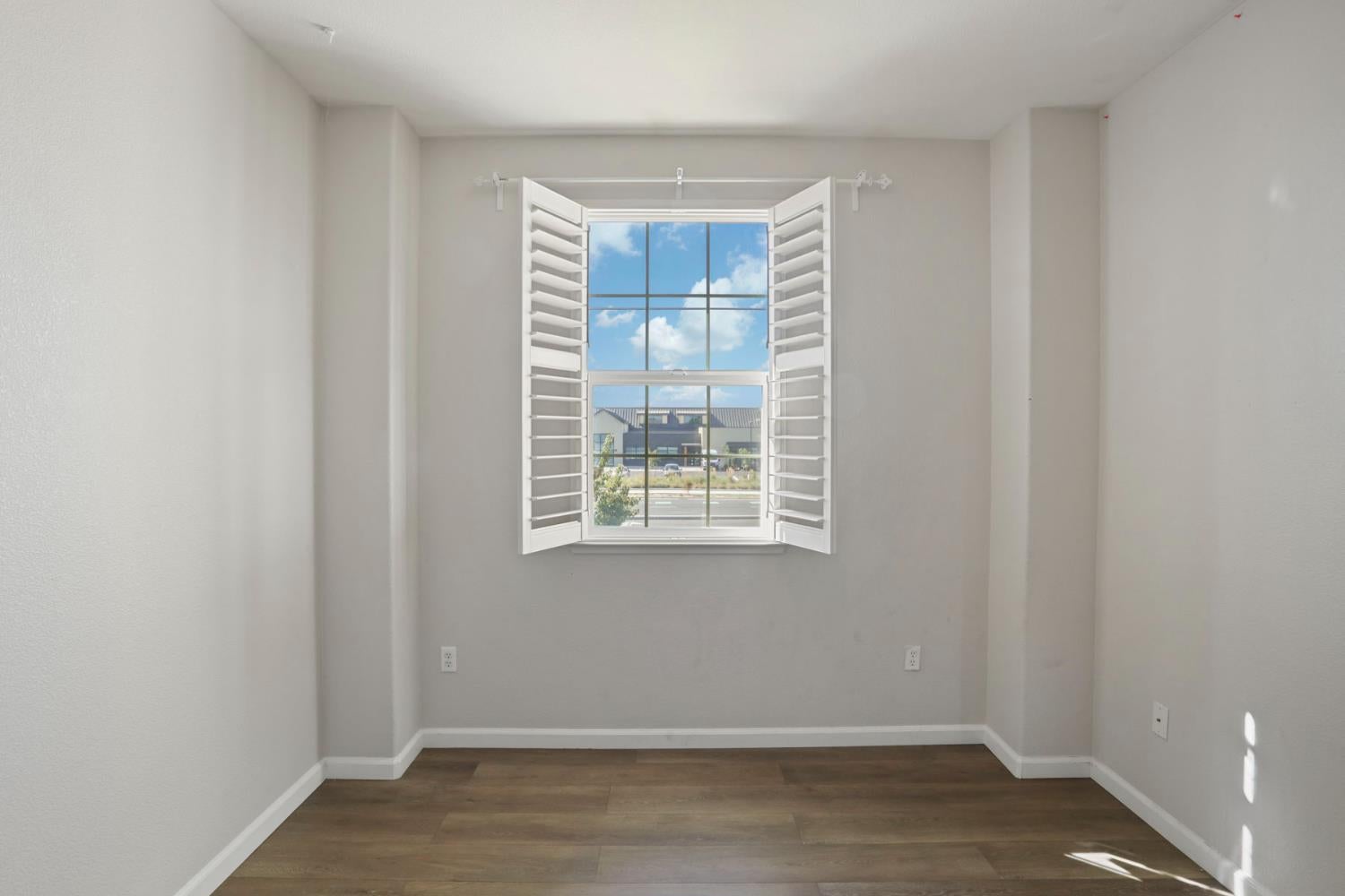 Empty room with dark wood-look flooring and a window with open white shutters.