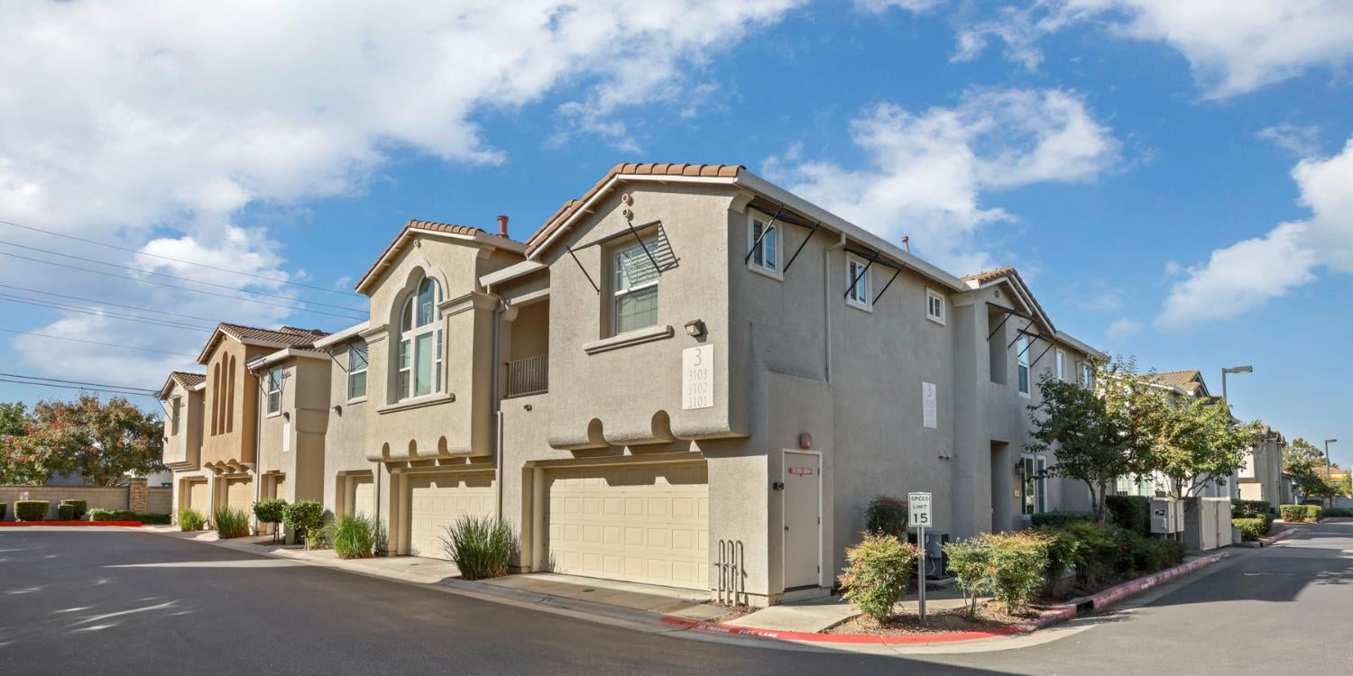 Multi-unit stucco residences with attached garages and arched windows along a paved drive.