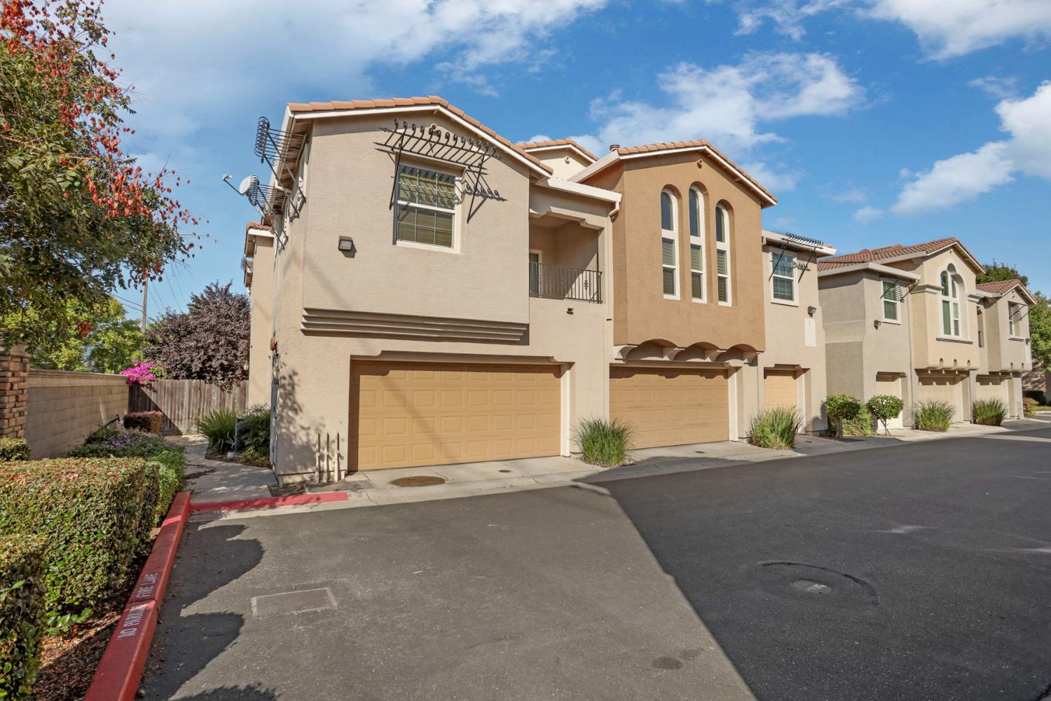 Tan two-story townhomes with arched windows and attached garages along a paved drive.