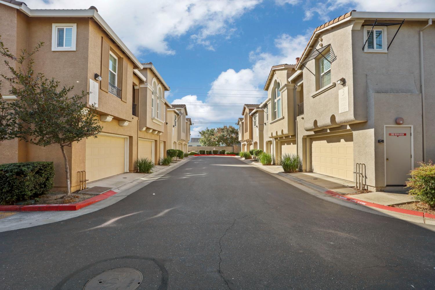 Lane between tan two-story townhomes with attached garages and red fire-lane curbs.