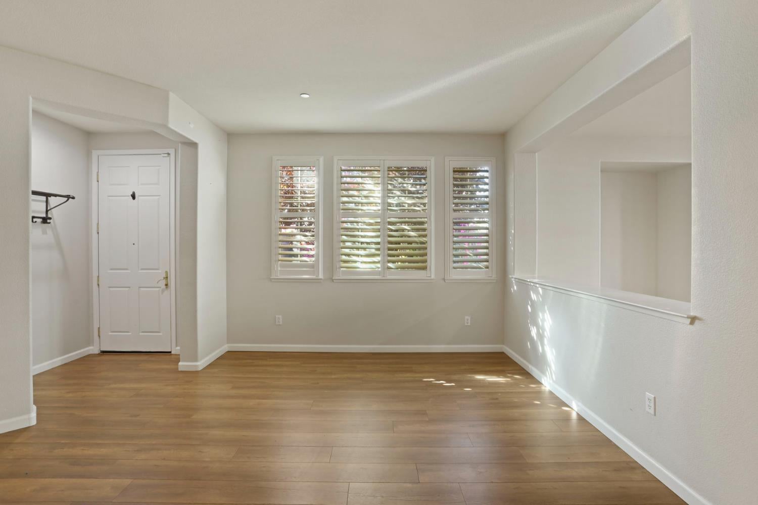 Empty room with wood floors, plantation shutters, and a wide pass-through opening.