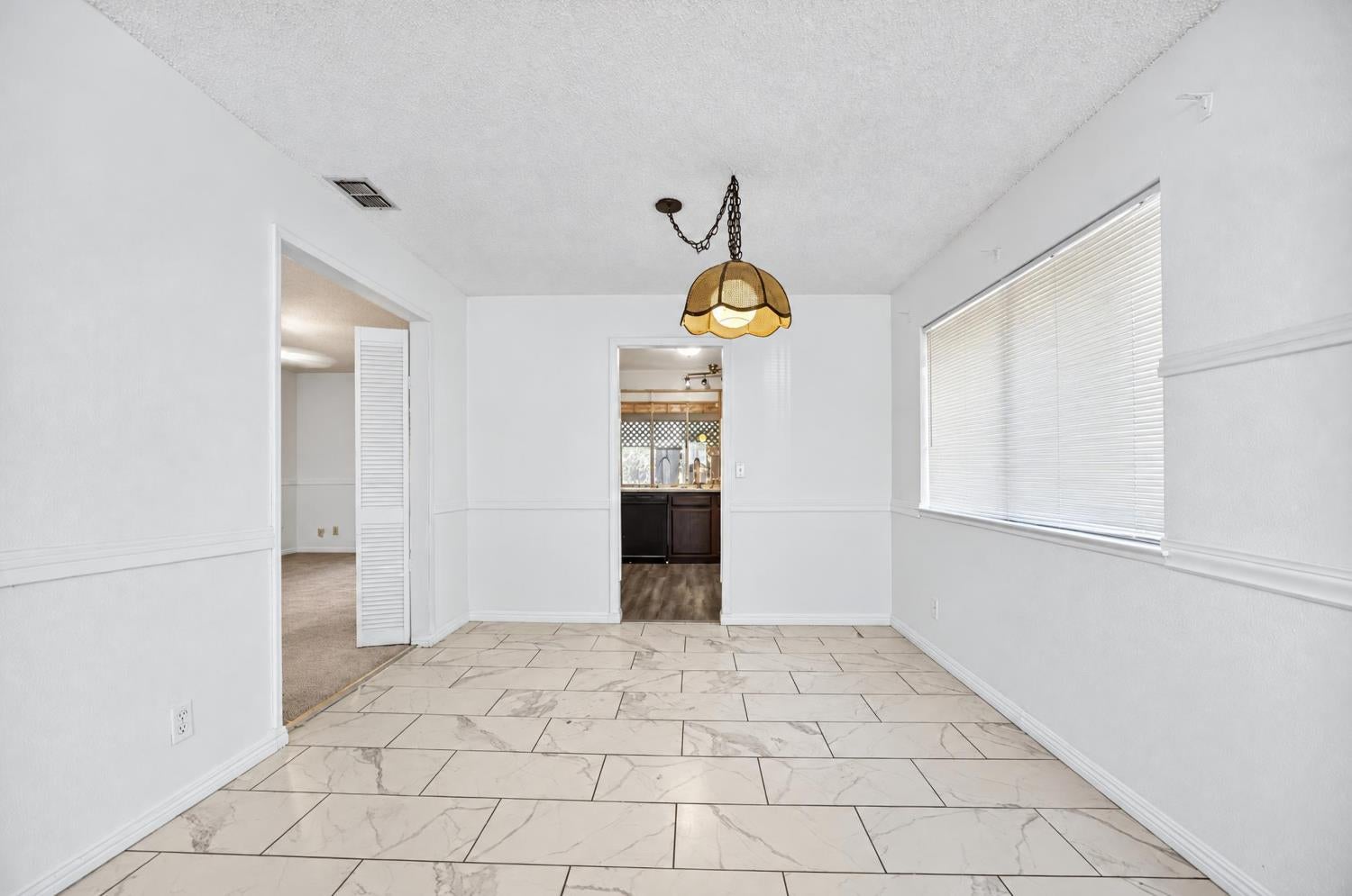 Empty dining room with large tile flooring, a pendant light, and a window with blinds.