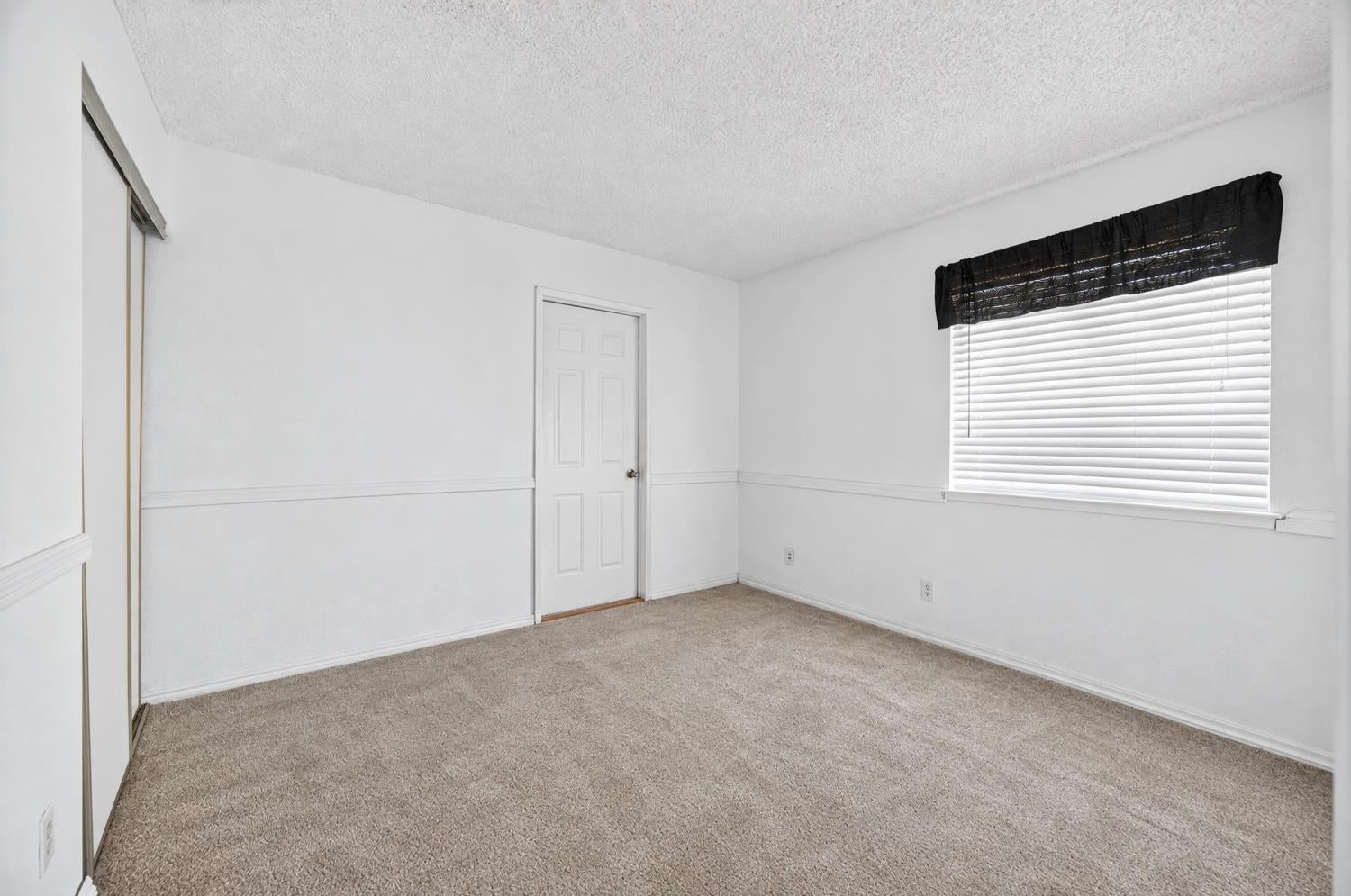 Empty bedroom with beige carpet, a sliding-door closet, and a window with blinds.