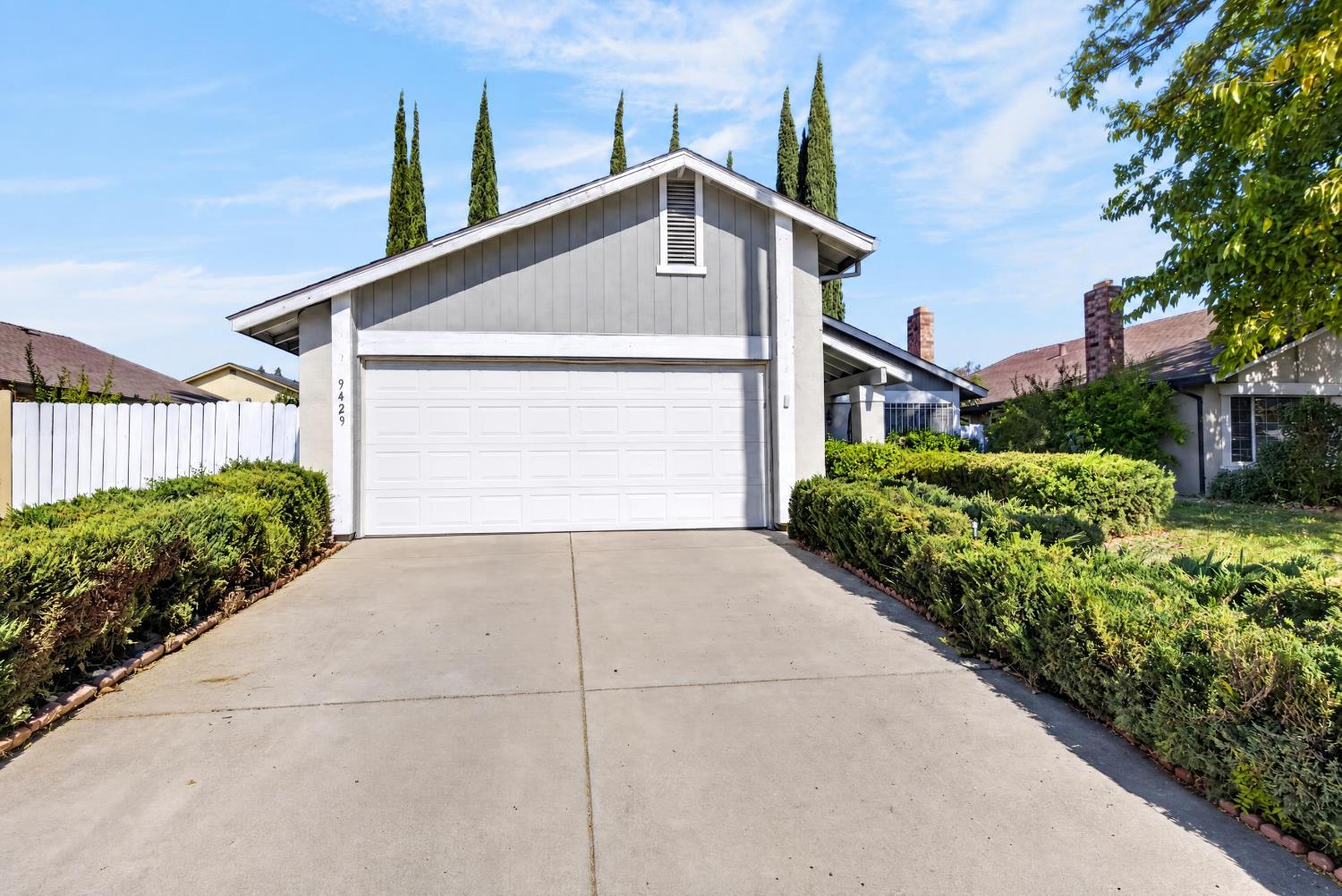 Gray home with a white double garage, broad driveway, and trimmed hedges.