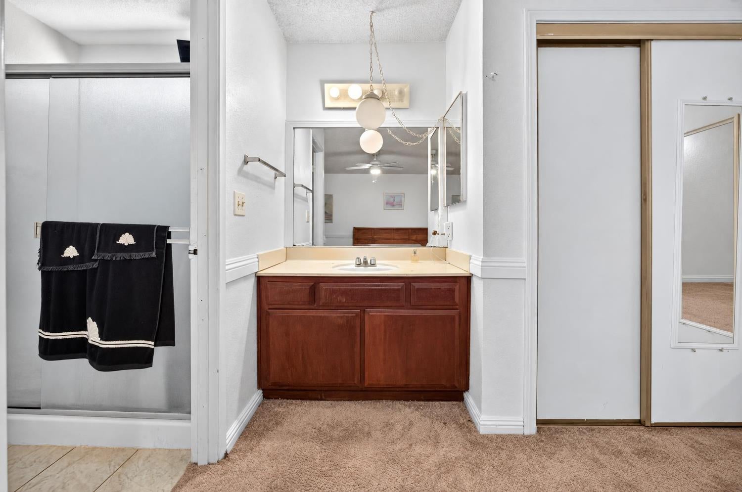Bathroom vanity with dark wood cabinets and a mirrored wall beside a shower with black towels.
