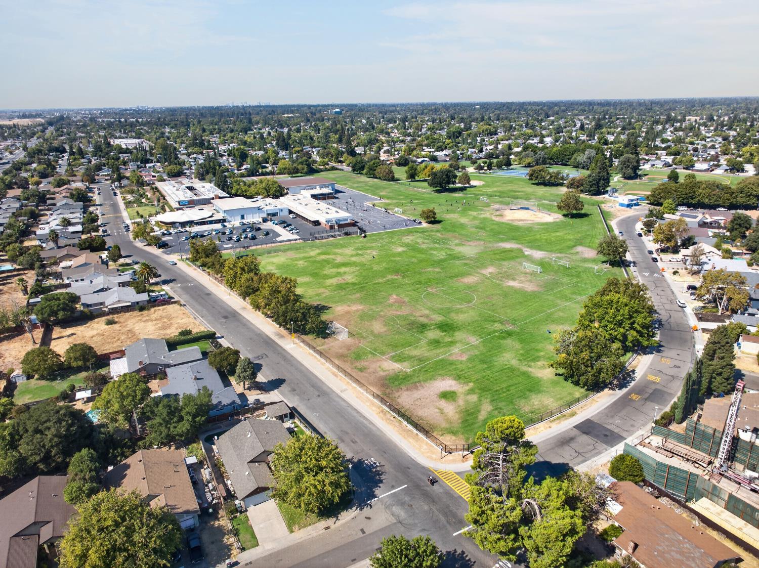 Aerial view of a neighborhood sports field and school campus surrounded by homes and tree-lined streets.