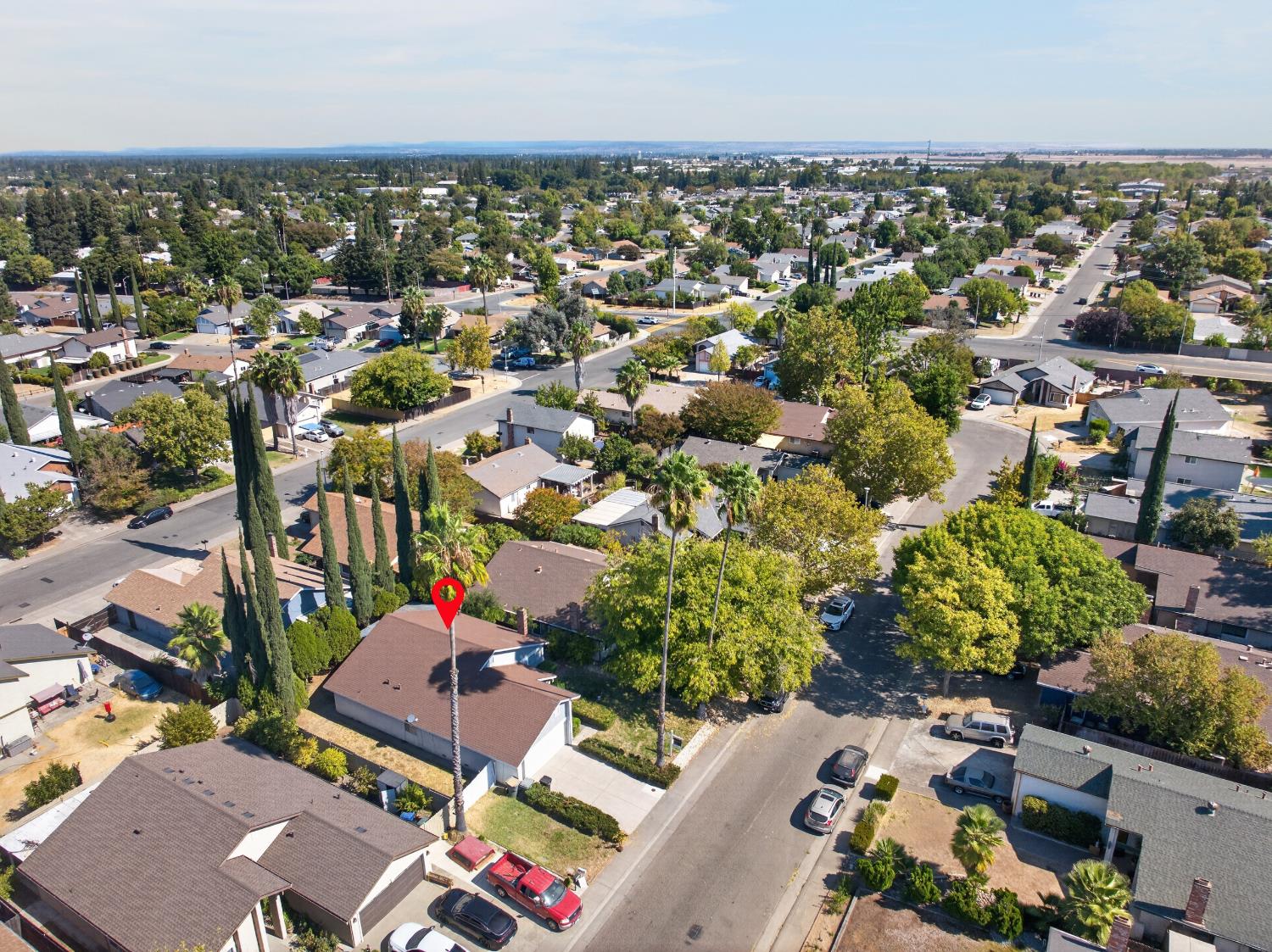 Aerial neighborhood view with a red pin marking a home among tree-lined streets.