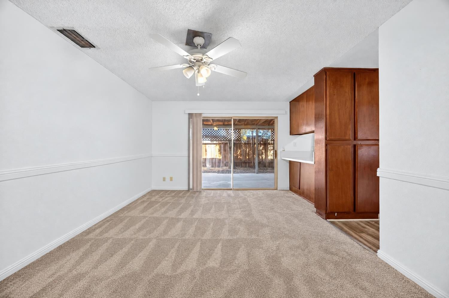 Empty carpeted living area with built-in wood cabinetry and a sliding glass door to the patio.