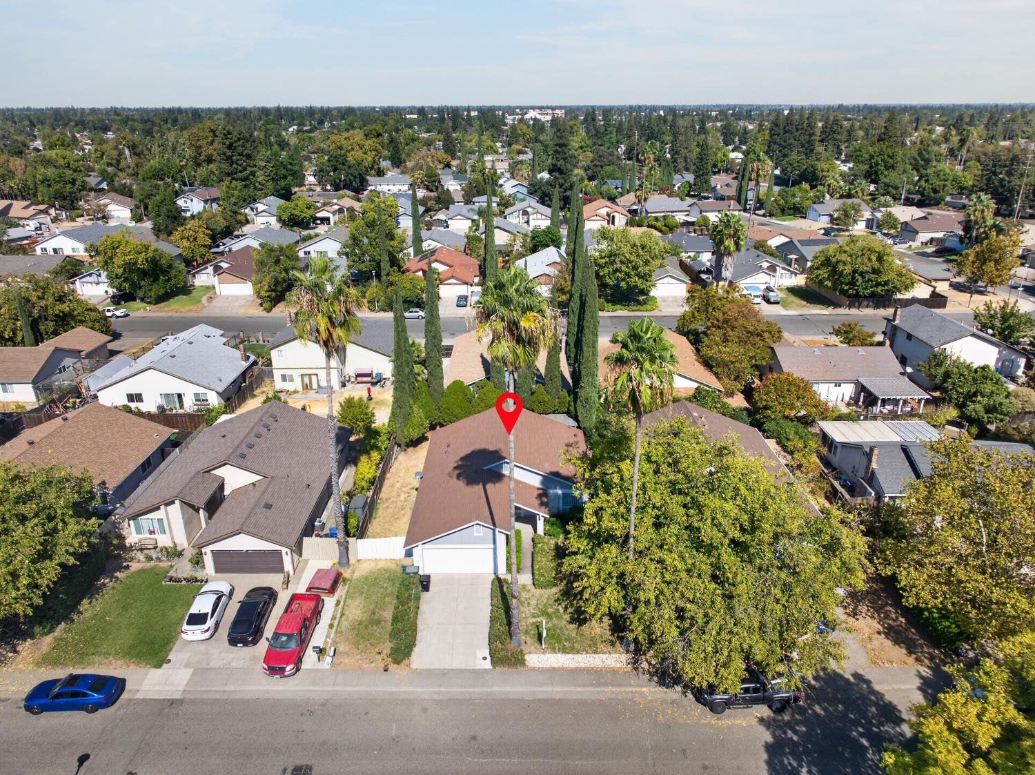 Aerial view of a blue-gray home with a brown roof, marked among leafy neighborhood homes.