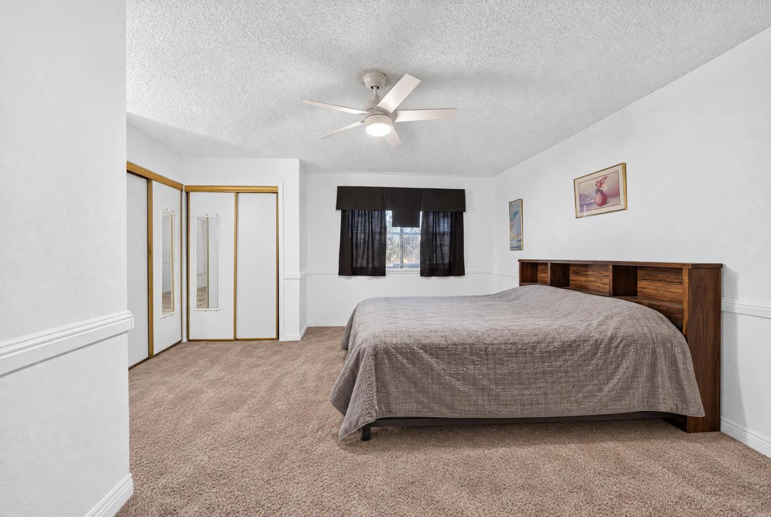 Bedroom with a large bed, mirrored closet doors, beige carpet, and ceiling fan.