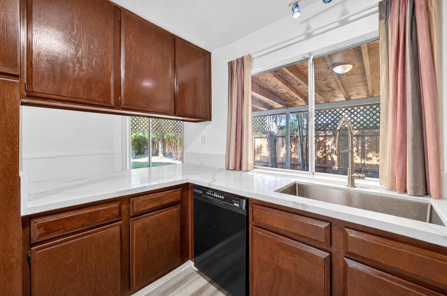 Kitchen with dark wood cabinets, white counters, and a deep sink beneath a backyard-facing window.